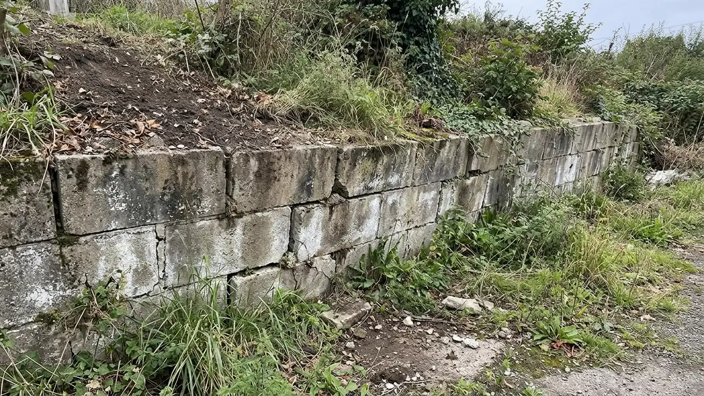 Before: a retaining wall with a leaning segmental block retaining wall with cracked caps and mud stains at the base